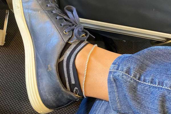 Une cheville avec un bracelet fin, une chaussette rayée et une basket usée.