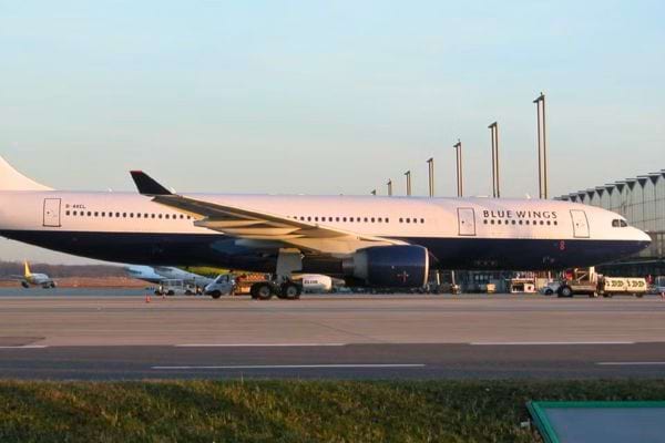 Avion Blue Wings stationné devant un terminal moderne au coucher du soleil.