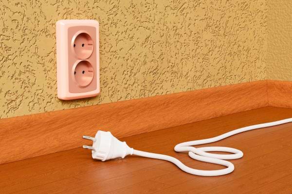 Prise murale vide avec un câble blanc débranché au sol.