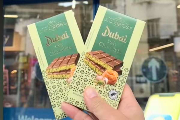 Deux tablettes de chocolat "Dubai Style" de J.D. Gross, tenues devant une vitrine.