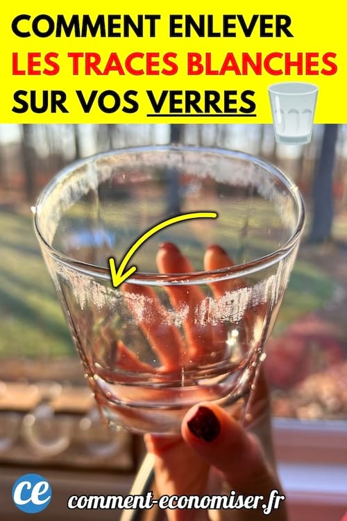 Une main tenant un verre transparent recouvert de traces blanches dues au calcaire.