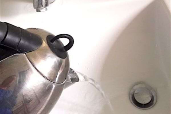 de l'eau bouillante versée dans un lavabo pour déboucher la canalisation