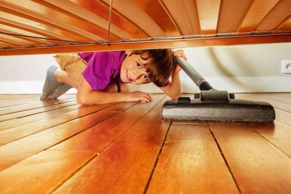 Enfant nettoie sous le lit avec un aspirateur.