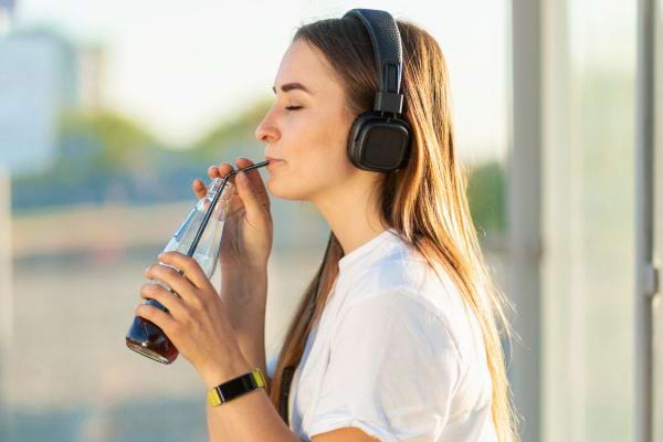 Femme buvant du Coca-Cola avec des écouteurs, en ville.