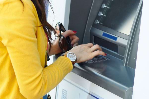 Femme en veste jaune tapant son code sur un distributeur automatique.