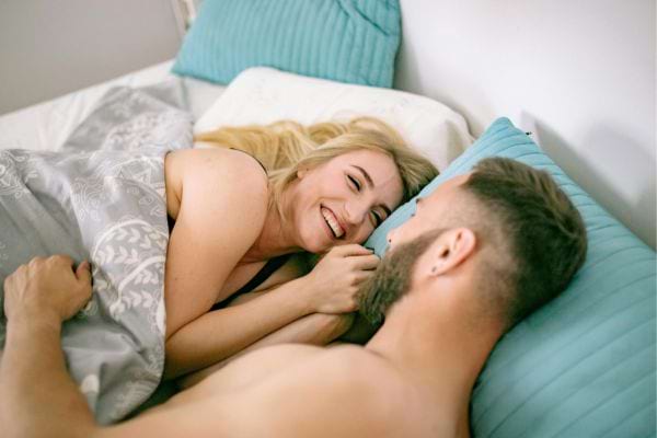 Une femme blonde rit en regardant son compagnon allongé à ses côtés.