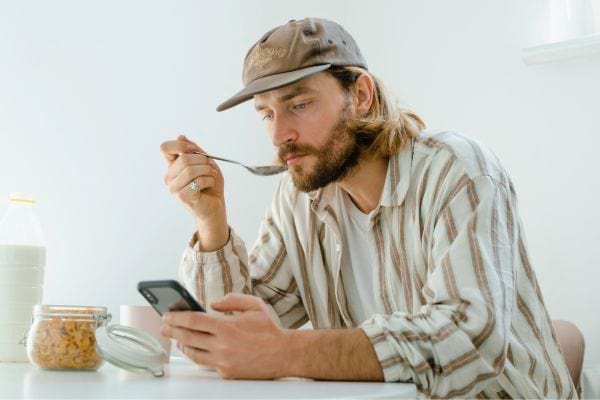 Homme mangeant tout en regardant son téléphone.