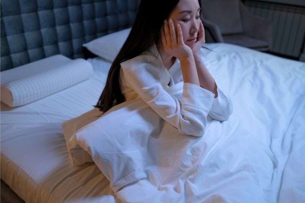 Femme en pyjama insomniaque assise dans son lit.