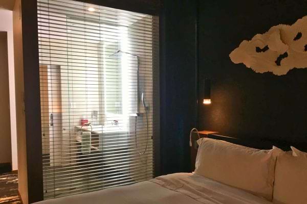 Chambre d'hôtel avec lit blanc, fenêtre et lumière tamisée.