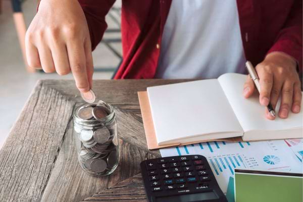 Pièces dans un bocal près d’un carnet et d’une calculatrice.