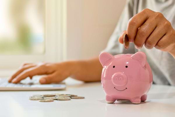 Personne économisant sur un bureau avec tirelire et pièces.