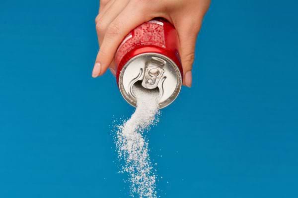 Main tenant une canette rouge, versant du sucre en poudre.