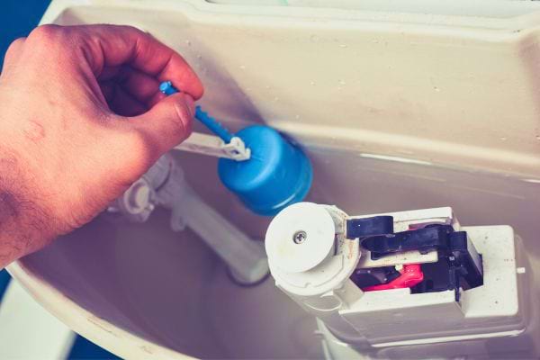Main réglant un flotteur dans une chasse d’eau.