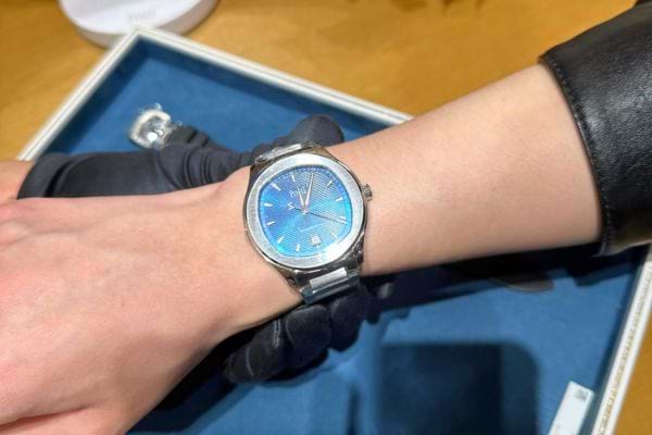 Montre bleue métallique portée sur gants noirs.