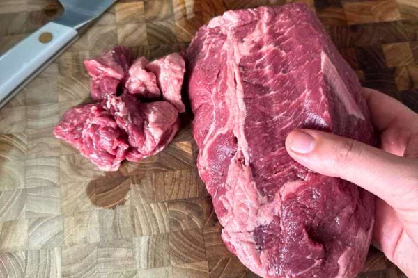 Un gros morceau de viande rouge tenu à la main, prêt à être découpé.