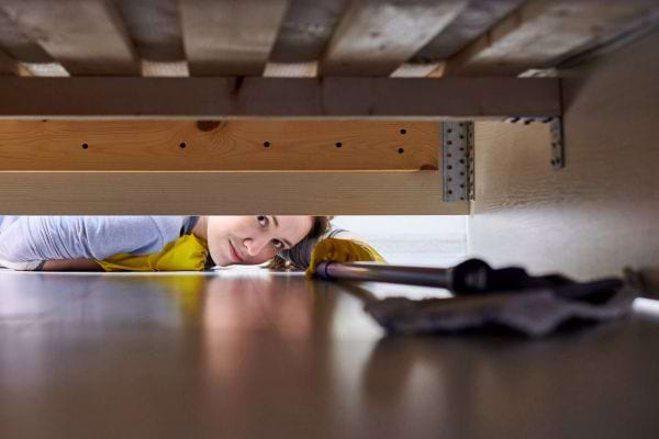 Femme regarde sous un lit avec un chiffon.