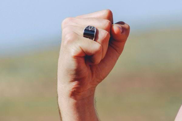 Poing fermé d’un homme avec une bague noire imposante sur l’index droit.