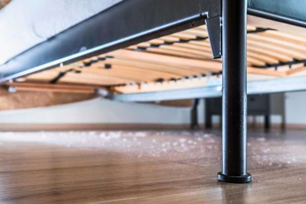 Sol sous un lit rempli de poussière visible.