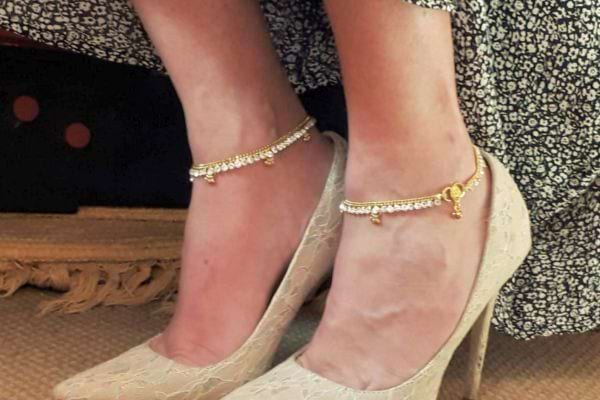 Deux chevilles ornées de bracelets dorés avec breloques, portés avec des talons en dentelle.