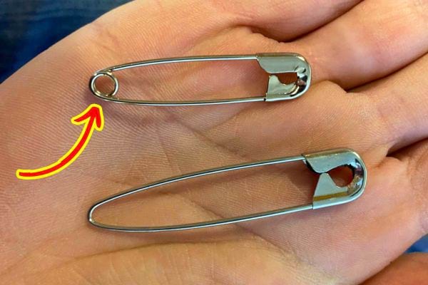 Deux épingles à nourrice posées sur une main, l'une avec un trou bien visible à l'extrémité.