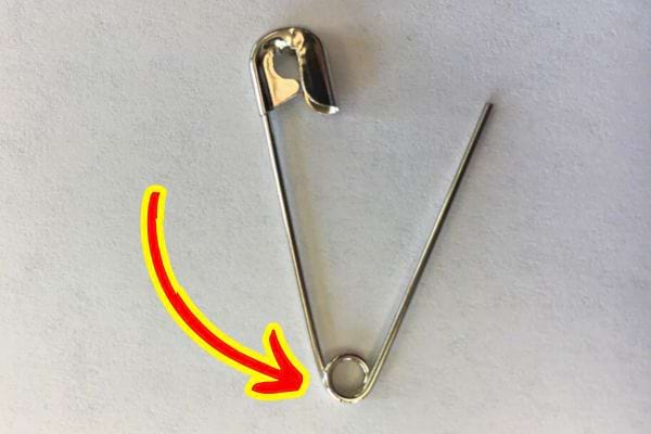 Une épingle à nourrice ouverte sur fond blanc, mettant en évidence le petit trou rond à sa base.