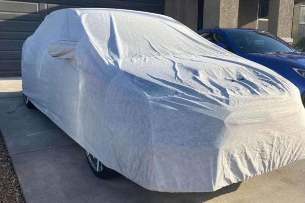 Voiture protégée sous une housse extérieure blanche.
