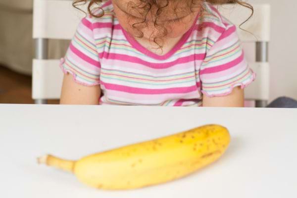 Enfant boude devant une banane posée sur la table.