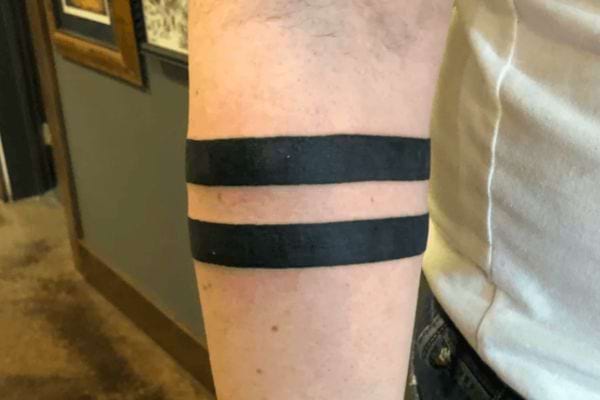 Deux larges bandes noires parallèles tatouées sur l’avant-bras.