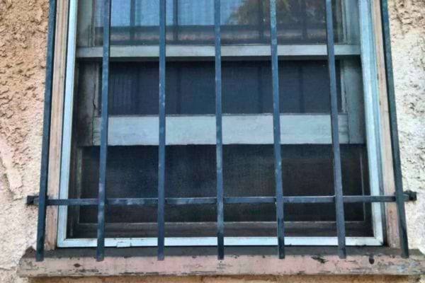 Barreaux verticaux droits, sans ornement, sur vieille fenêtre.