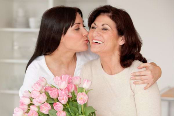 Fille embrasse sa mère, bouquet de tulipes roses en main.