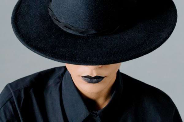 Personne en noir avec grand chapeau couvrant les yeux.