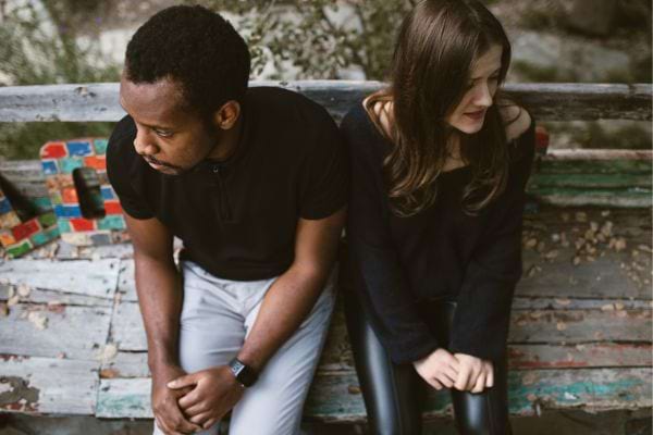 Un couple assis sur un banc, regardant dans des directions opposées, l’air distant.