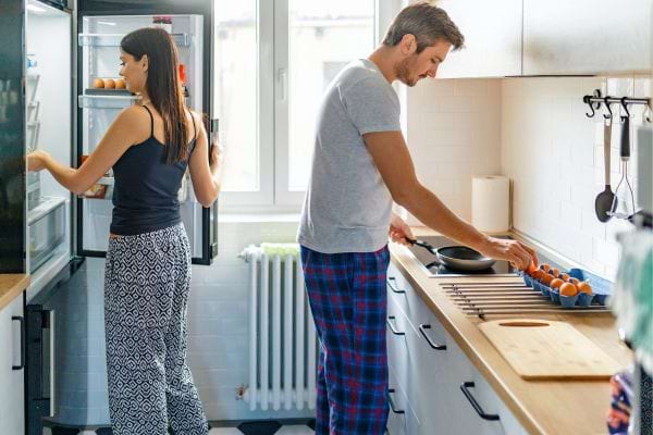 Couple en pyjama préparant le petit-déjeuner dans une cuisine lumineuse.