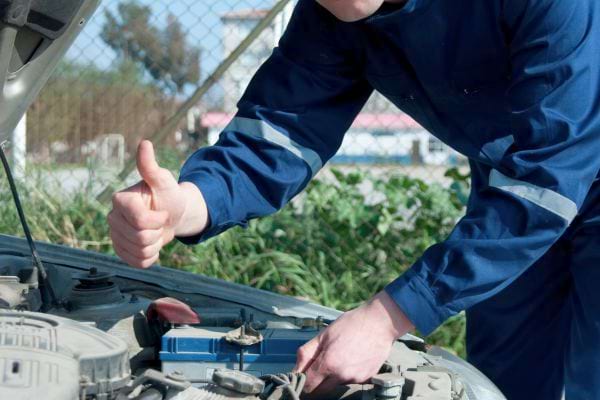 Mécanicien souriant fait un pouce levé devant un moteur.