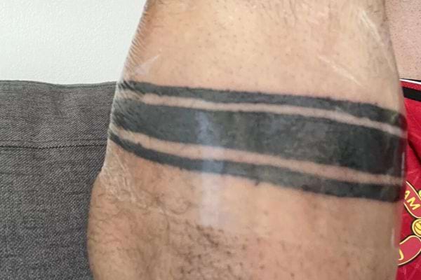 Tatouage de trois bandes noires irrégulières sur un bras musclé.