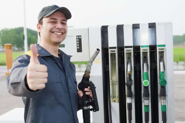 Un pompiste souriant fait un pouce levé à la station.