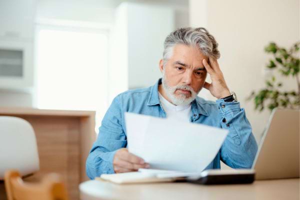 Homme inquiet lit une facture devant son ordi portable.