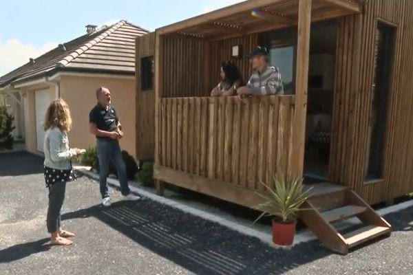 Une famille discute devant un petit studio en bois installé près d’une maison.