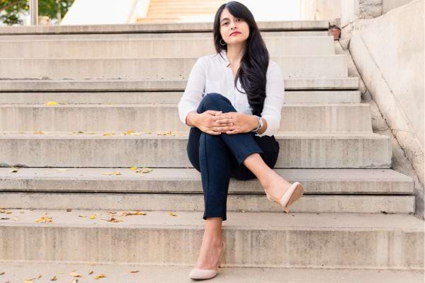 Femme en chemise blanche assise sur des marches, jambes croisées.