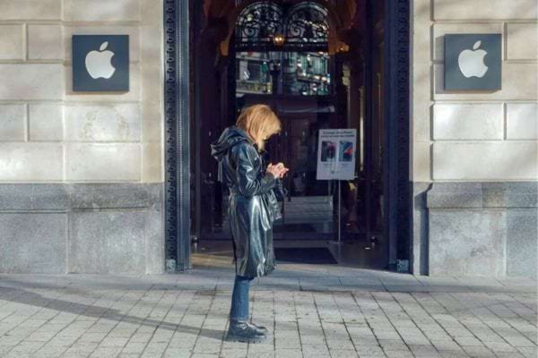 Femme concentrée sur son iPhone devant un magasin Apple.
