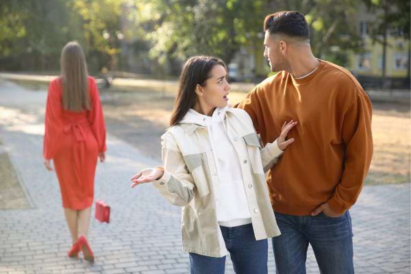 Femme énervée face à un homme regardant une autre.