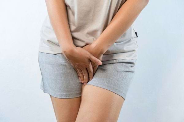 Femme en short tenant ses parties intimes avec gêne.