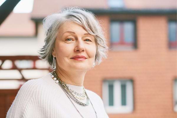 Femme mature aux cheveux gris souriant en extérieur.
