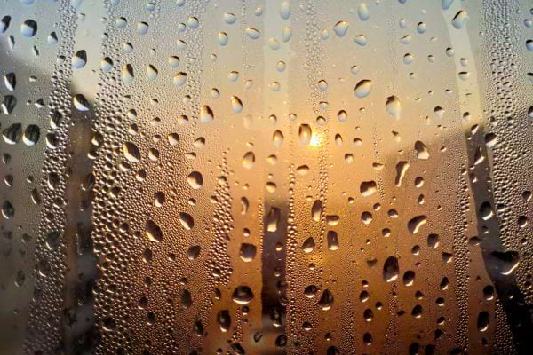 Gouttes de pluie sur vitre avec lumière de coucher de soleil.