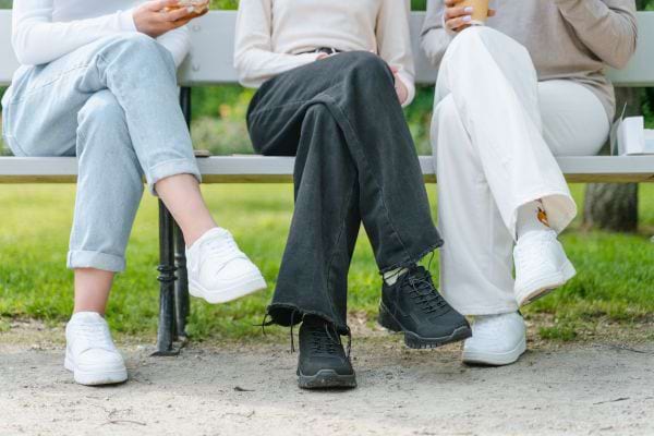 Trois femmes assises sur un banc, jambes croisées et baskets.