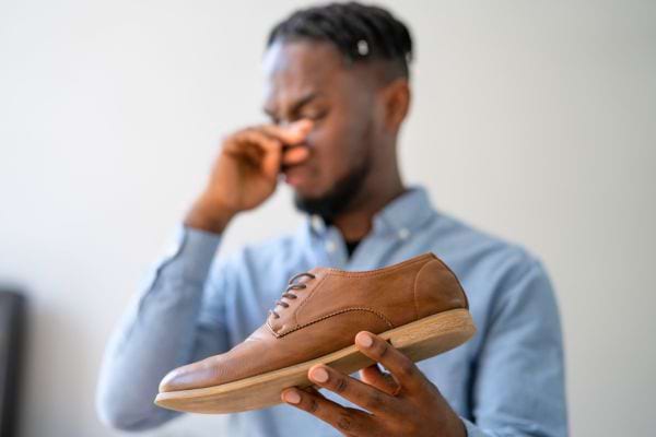 Un homme grimace en tenant une chaussure malodorante.