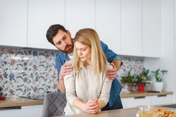 Un homme enlace une femme triste dans la cuisine.