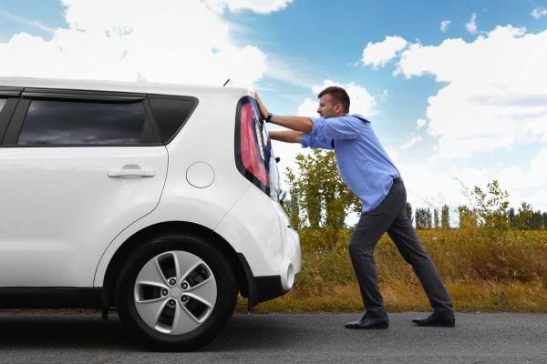 Homme poussant une voiture blanche en panne sur la route.