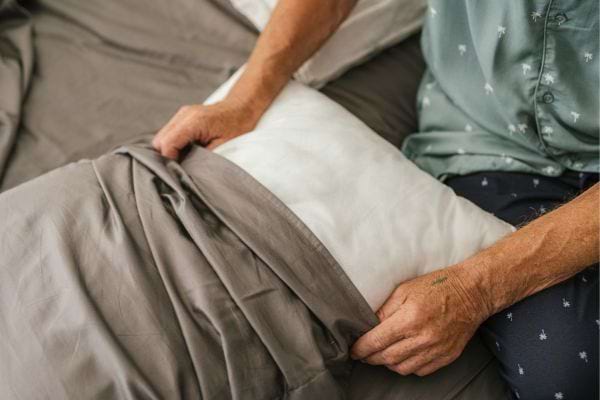 Un homme en pyjama remet une taie sur son oreiller.