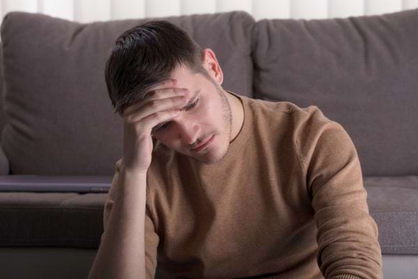 Un jeune homme seul, assis, la main sur le front, visiblement accablé.